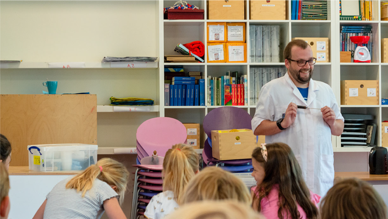 An instructor standing in front of shelving, teaching kids about science.