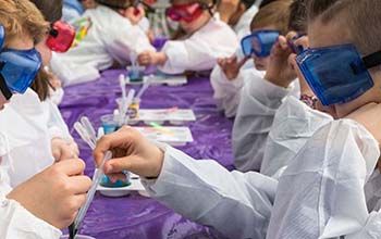 Kids wearing safety goggles pouring liquid into a mad science cup using a pipette