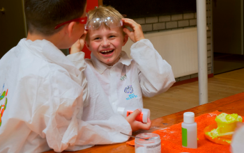 Two boys smiling at each other while wearing lab glasses and doing chemistry experiments.