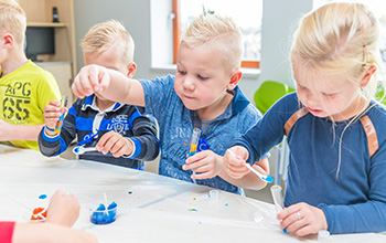 3 kids putting blue and yellow substance in a test tube