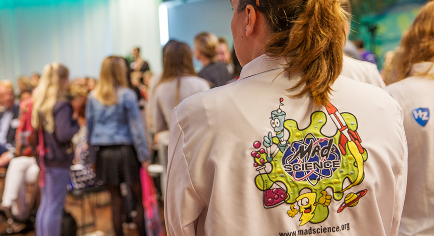 Mad scientist standing wearing a lab coat with the mad science logo on the back of the coat