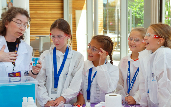 Kids in lab coats listening to an instructor.